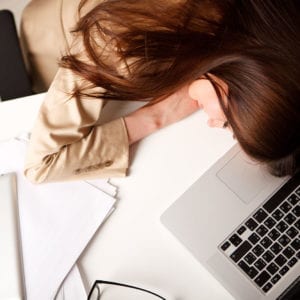 Woman asleep on her desk with laptop and paperwork in view.